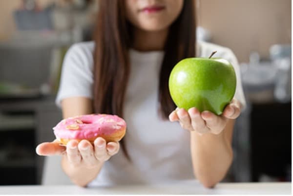 Photo of woman holding an apple in one hand and a doughnut in the other.